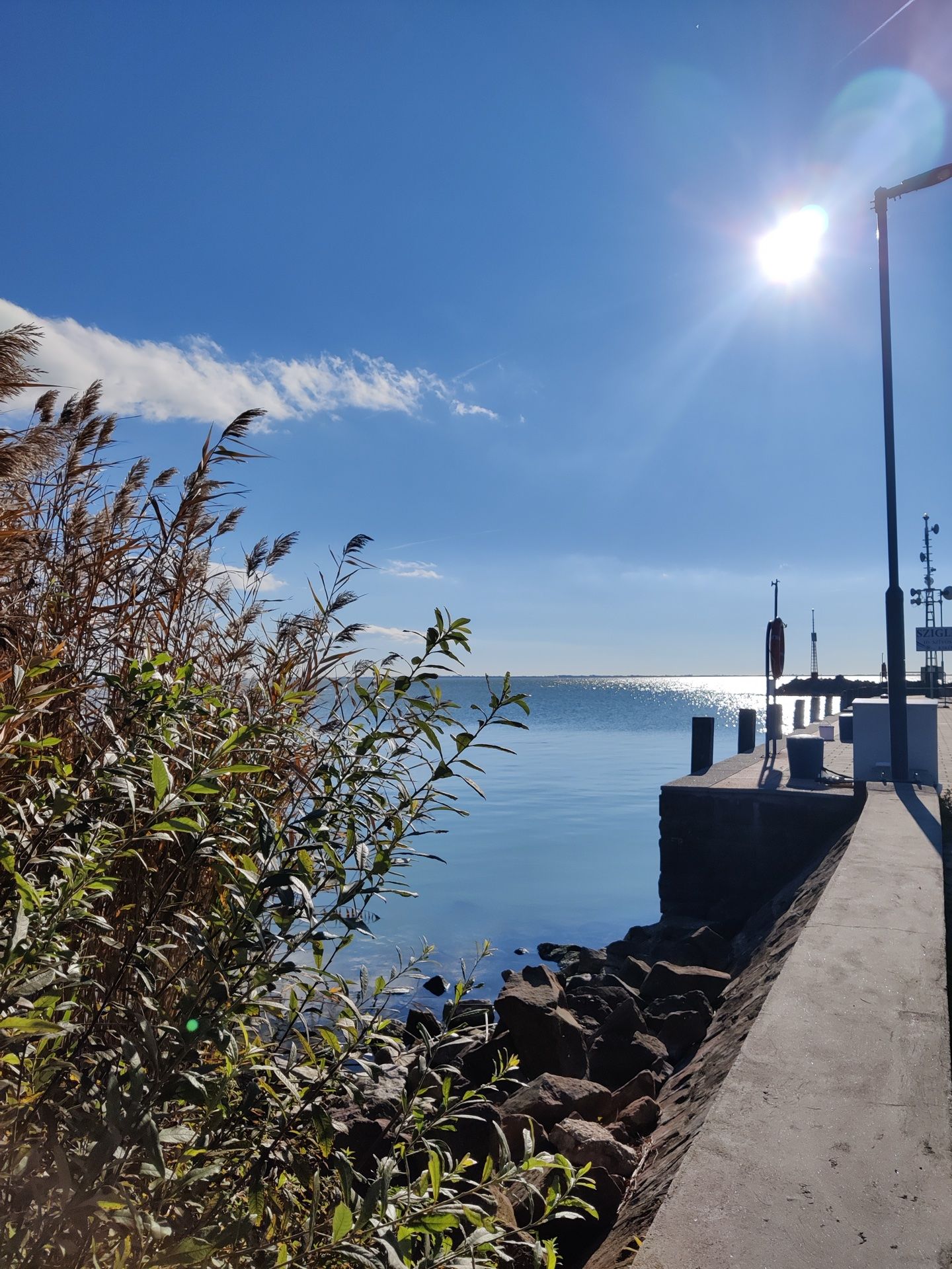 Blick auf eine steinige Küste und einen Hafen bei Sonnenschein mit blauem Himmel und wenigen Wolken.