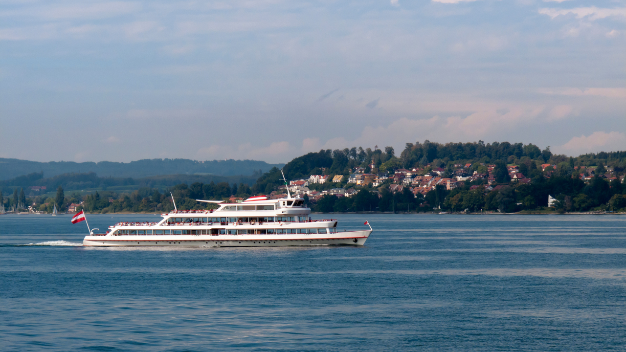 Hundeurlaub am Bodensee: Schifffahrt mit Vierbeiner Ausflugsschiff auf dem Bodensee mit Uferort und Waldkulisse, Hundereisen-Inspiration