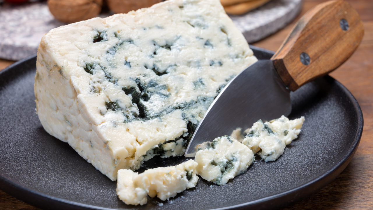 Blauschimmelkäse: Giftig für Hunde Blauschimmelkäse auf schwarzem Teller mit Messer - Warnung vor giftigen Lebensmitteln für Hunde