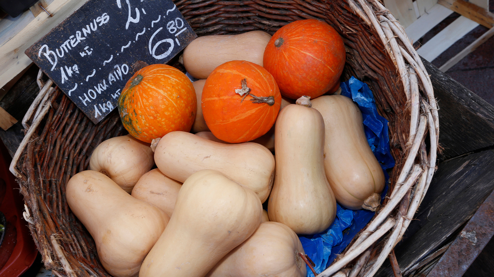 Korb mit orangenen Kürbissen und hellen Butternut-Kürbissen, geeignet als Hundenfutter