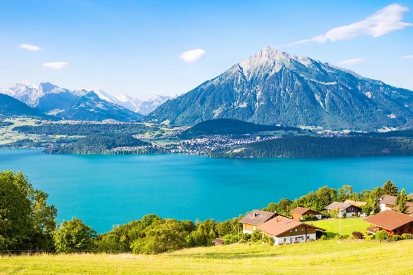 Blick über einen See auf einen majestätischen Berg und umliegende Landschaft mit Häusern.
