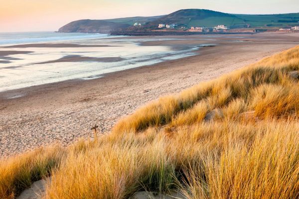 Ein weitläufiger Sandstrand in England mit Dünen und sanften Hügeln im Hintergrund bei Sonnenaufgang.