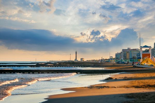 Weitläufiger Sandstrand von Jesolo bei Sonnenuntergang mit einem Leuchtturm im Hintergrund.