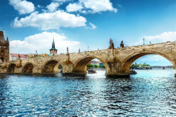 Historische Steinbrücke mit Statuen über einem Fluss, blauer Himmel im Hintergrund.