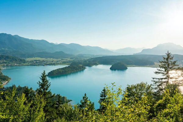 Blick auf einen See mit grünen Inseln und bewaldeten Ufern, umgeben von Bergen.